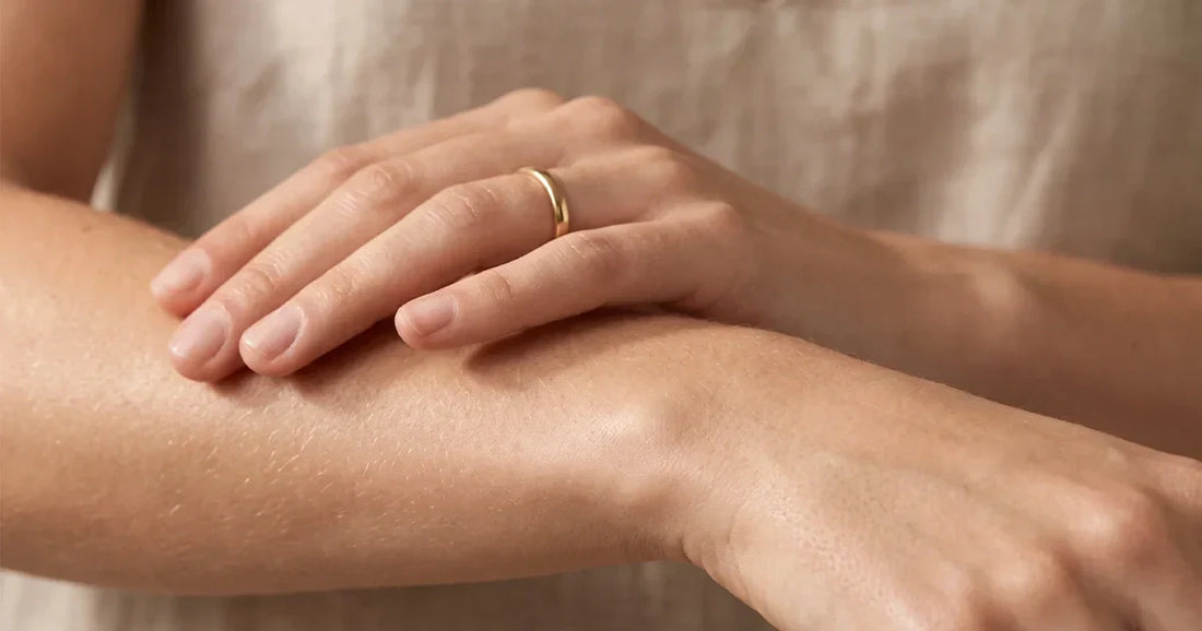 Primer plano de una mano tocando suavemente la piel del antebrazo, con luz natural cálida resaltando su textura saludable