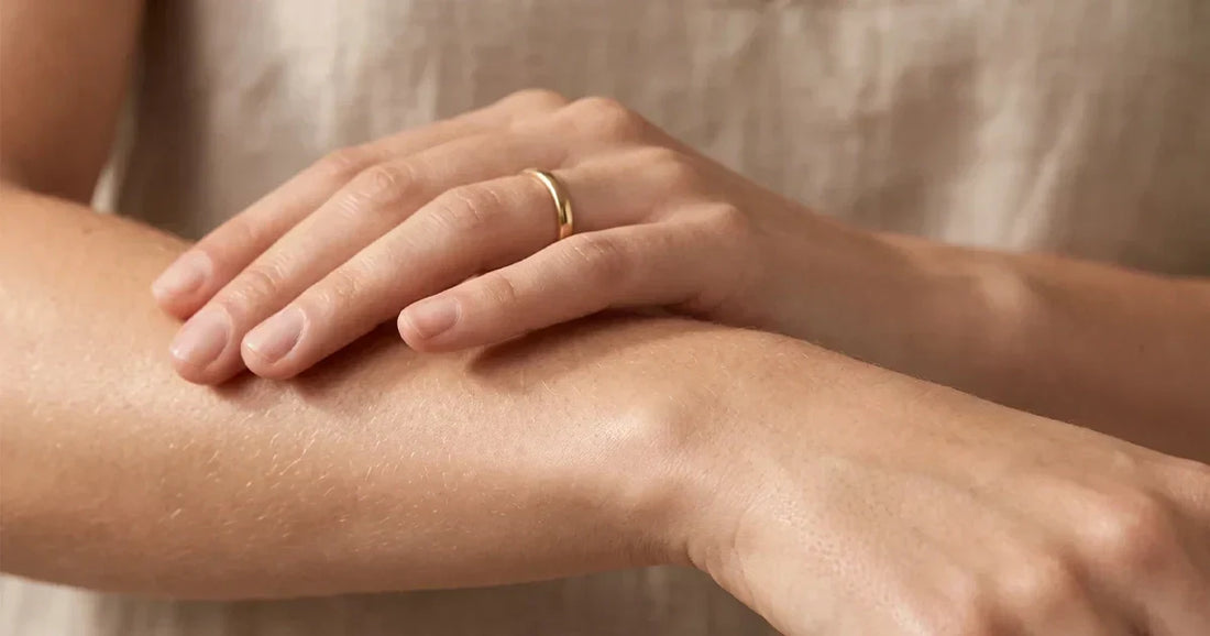 Primer plano de una mano tocando suavemente la piel del antebrazo, con luz natural cálida resaltando su textura saludable